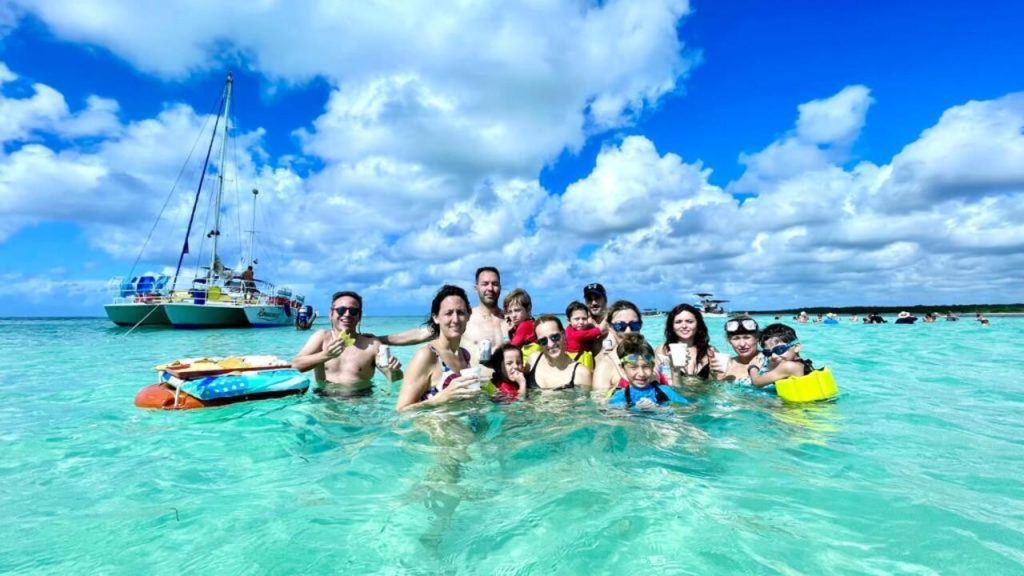 Group of travelers in shallow turquoise water next to a catamaran