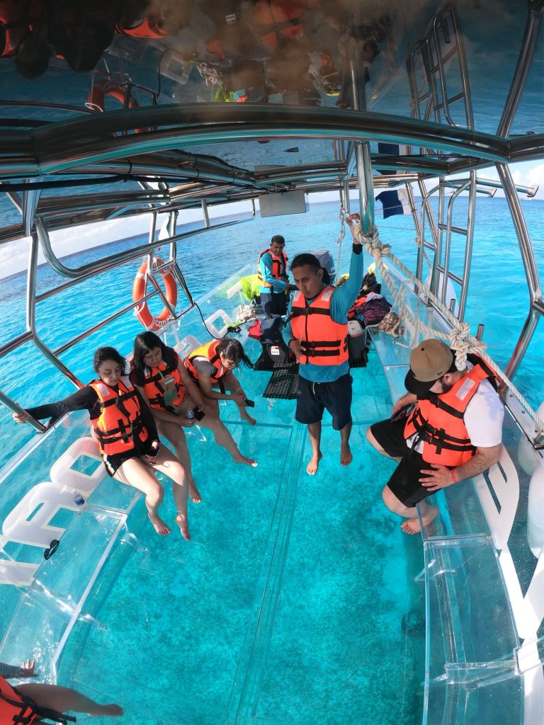 Travelers in life vests aboard a clear-bottom boat over turquoise water in Cozumel